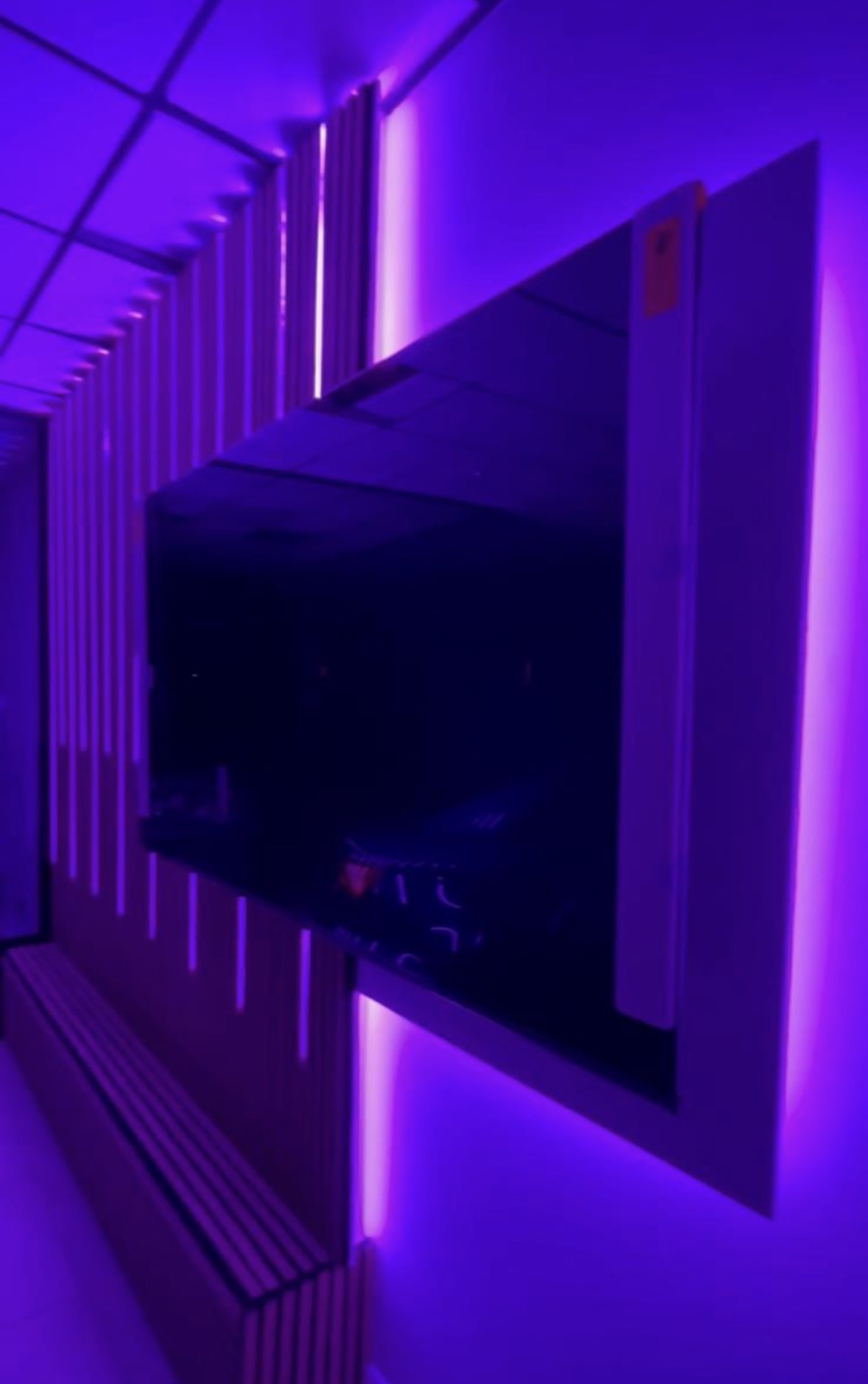 Wall-mounted display screen framed by colour-changing LED lighting and a lit slatted panel in a car showroom
