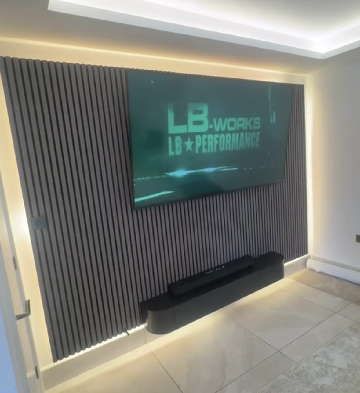 Dark slatted feature wall with a wall-mounted television, perimeter cove lighting and concealed floor-level LED