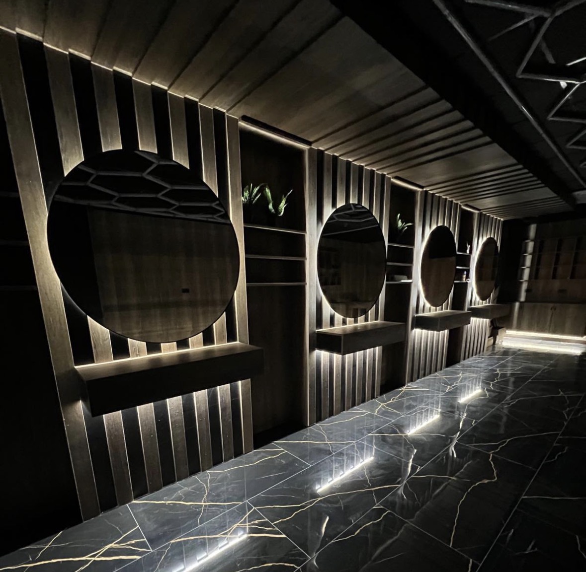 Commercial salon fit-out with a run of backlit round mirrors on a slatted timber wall and lit floating shelves