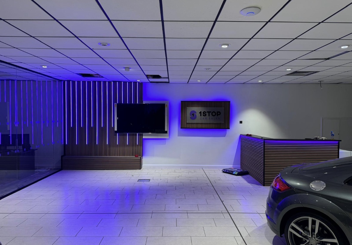 Car showroom reception with colour-changing LED battens set into a timber slat wall and a backlit brand sign