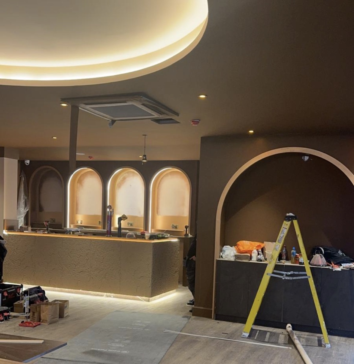 Commercial bar fit-out in progress with lit arched niches, a circular cove-lit ceiling detail and LED under the counter