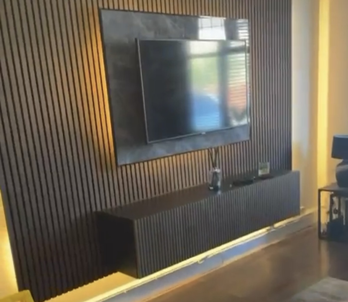 Slatted media wall with a floating unit and warm LED lighting washing the floor beneath it