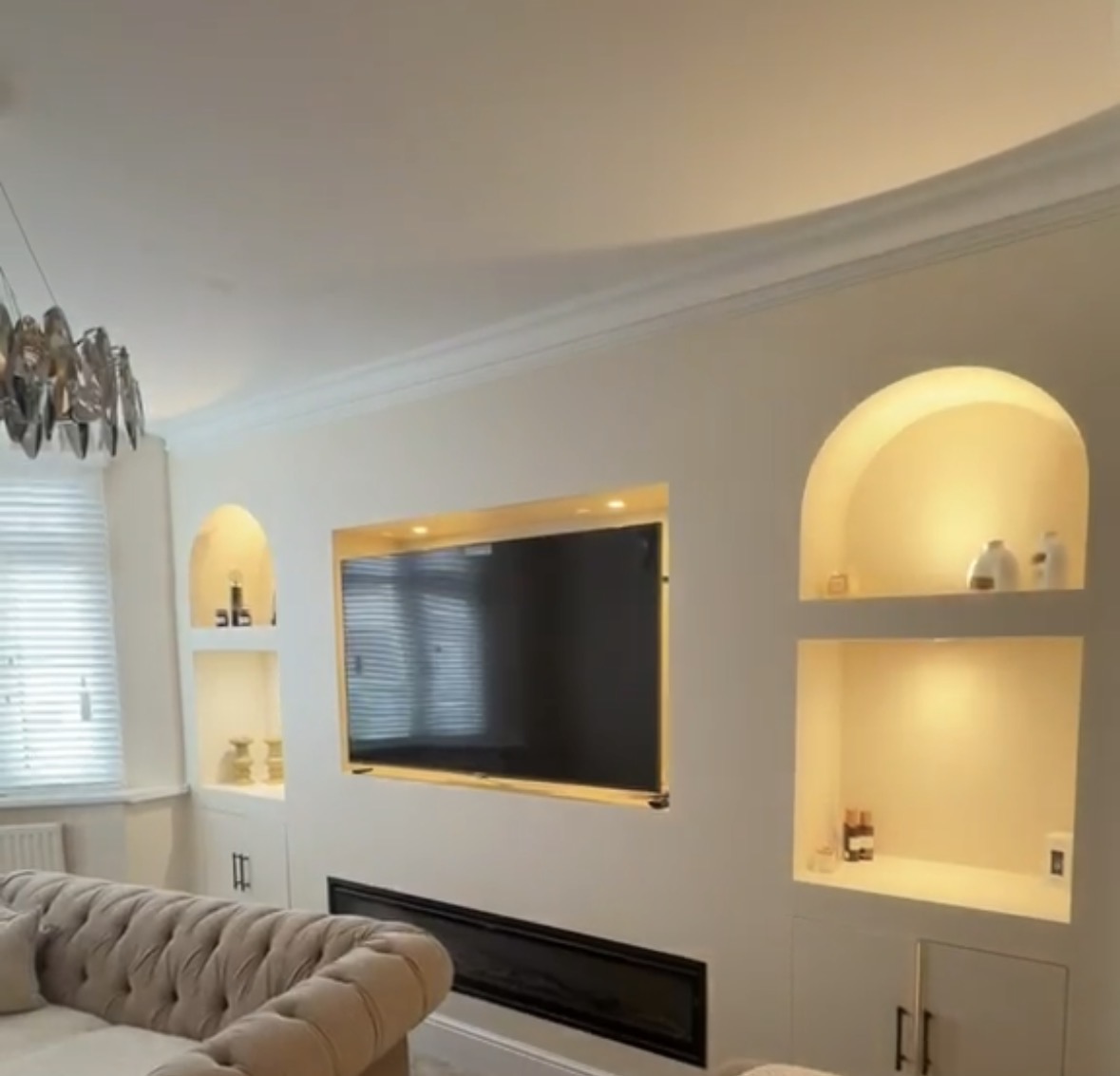 Living room media wall with a recessed television and arched alcoves lit with warm concealed LED lighting