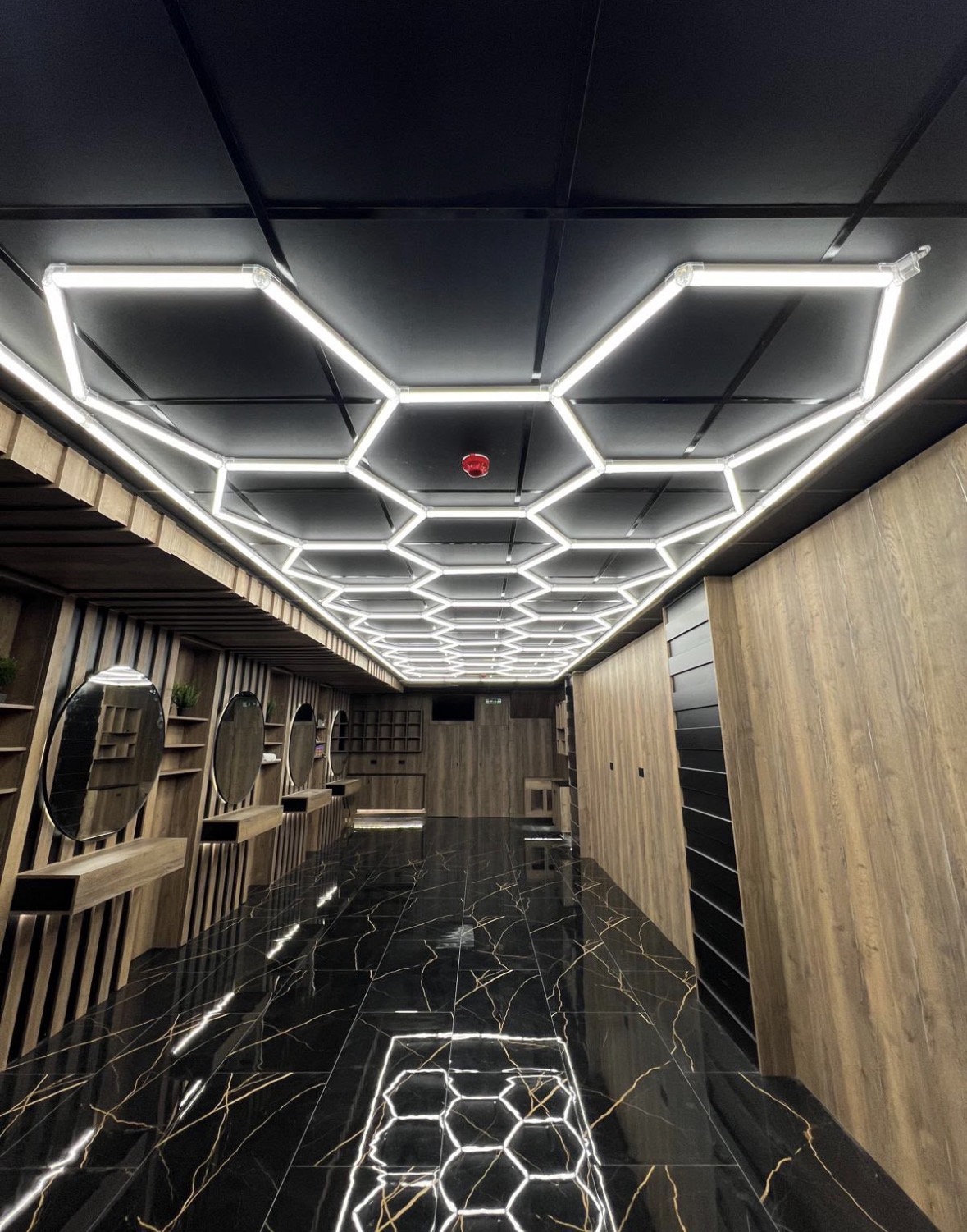 Hexagonal LED grid lighting installed across a black suspended ceiling above a salon floor