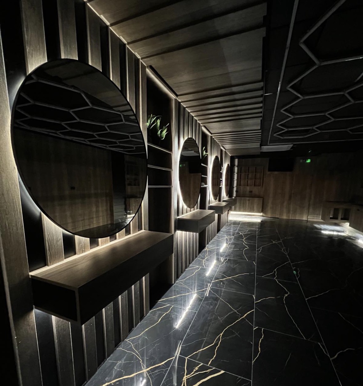 Backlit circular mirrors and concealed LED strips running along a dark slatted wall in a salon interior