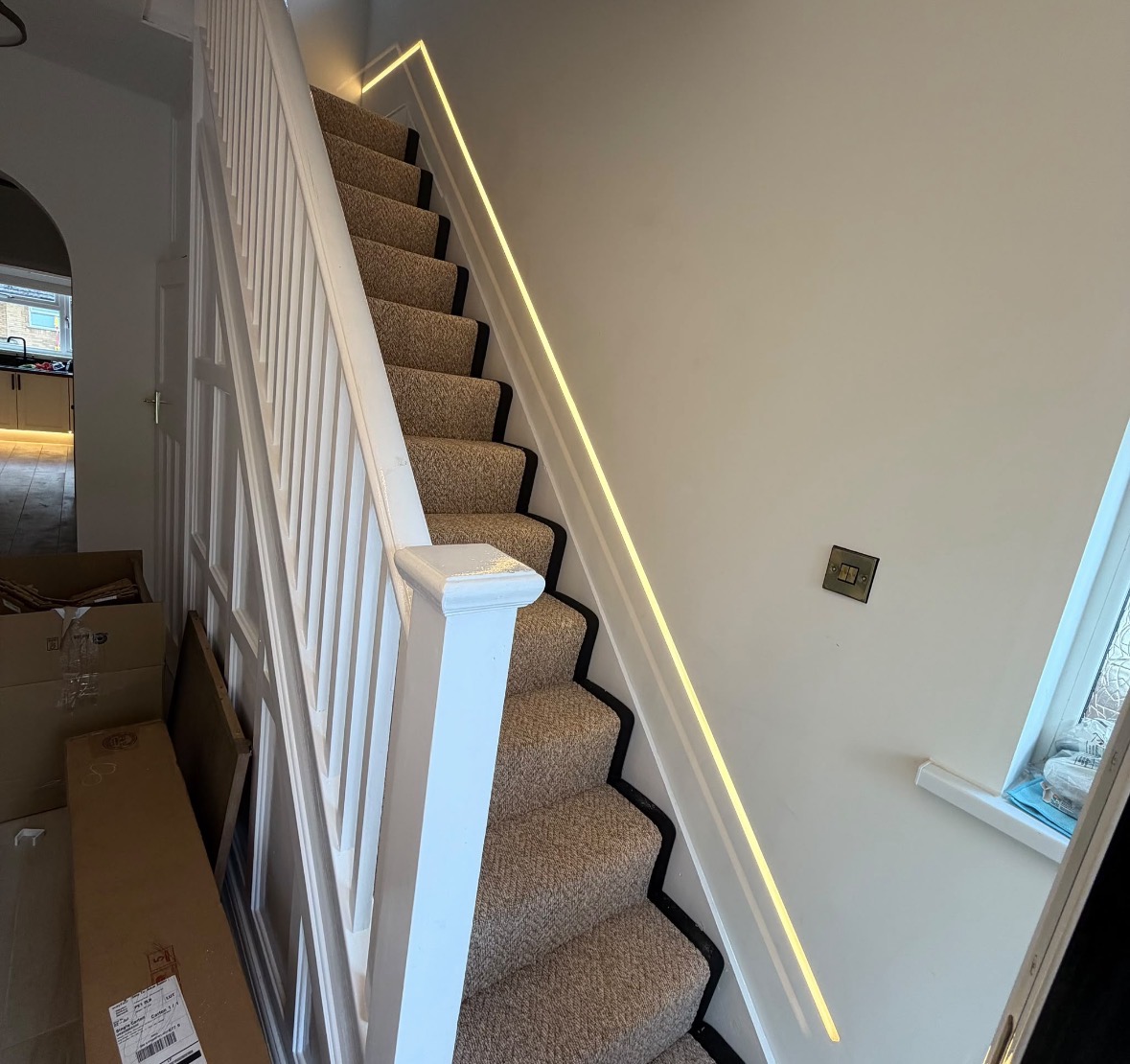 Hallway view of a staircase with linear LED lighting and a brushed brass light switch