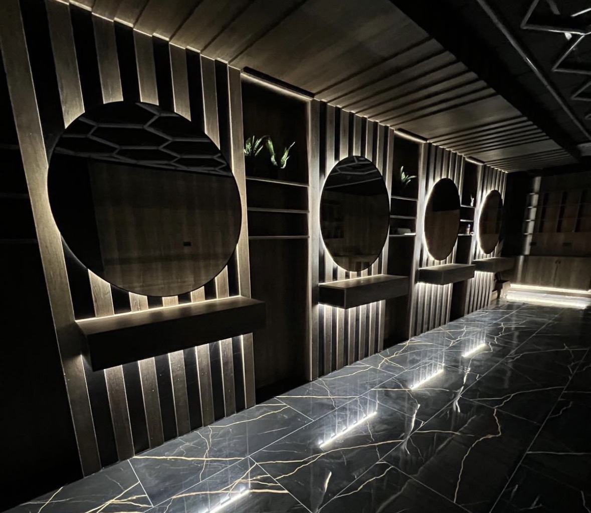 Row of illuminated mirror stations with concealed lighting behind timber battens and lit shelving