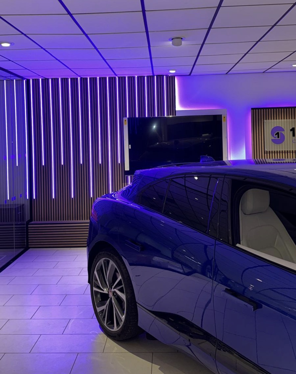 Vertical LED light battens in a showroom feature wall reflecting off a parked car