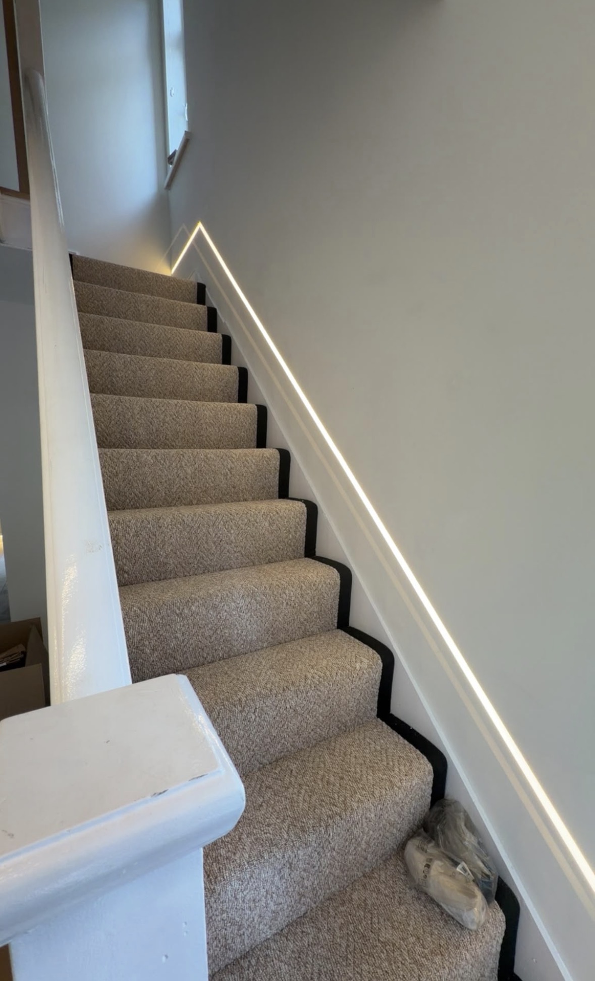 Warm white LED strip lighting recessed into a staircase wall, running the full rise of the stairs