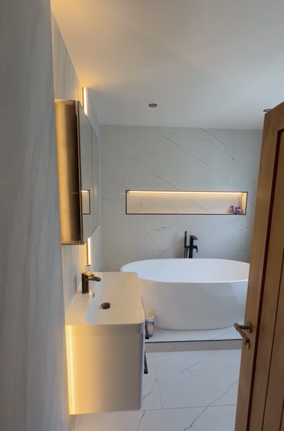 Bathroom with an illuminated tiled niche, lit mirror cabinet and recessed downlight above a freestanding bath
